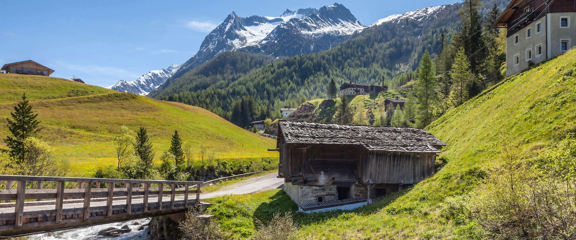 Mountain world Ahrntal Several mountain huts in mountain landscape with stream and wooden bridge.