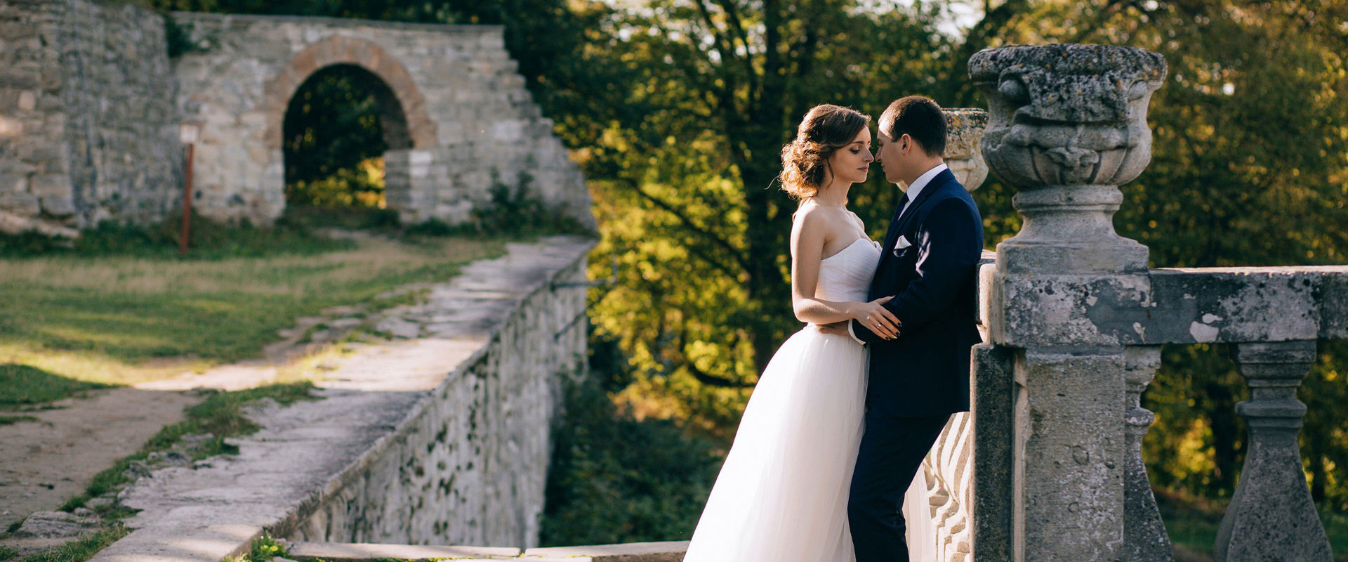 Freshly married couple A man in a suit and a woman in a wedding dress stand in a park and embrace.