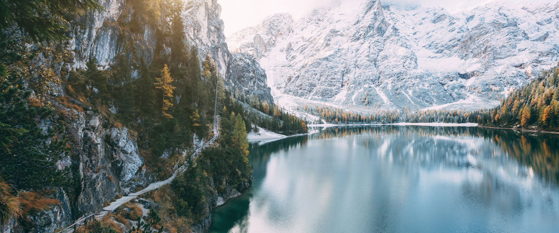 Deep blue mountain lake, surrounded by snow-covered mountains and forests. On the left side of the picture, a narrow path starts around the lake.