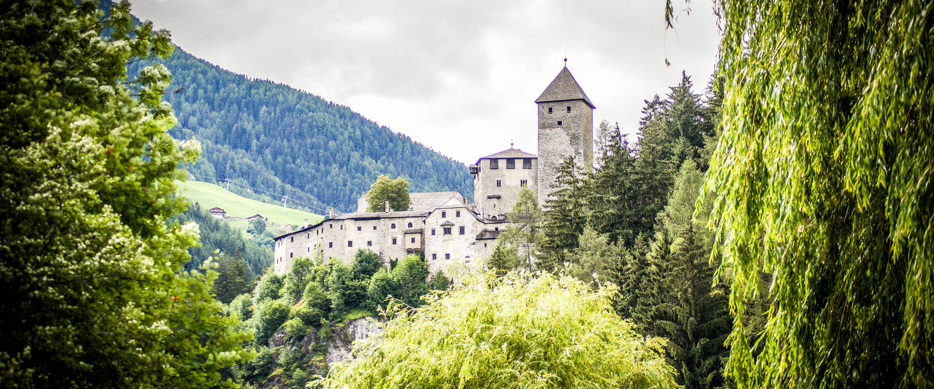 Taufers Castle sits enthroned on a steeply rising rocky hill, surrounded by trees.