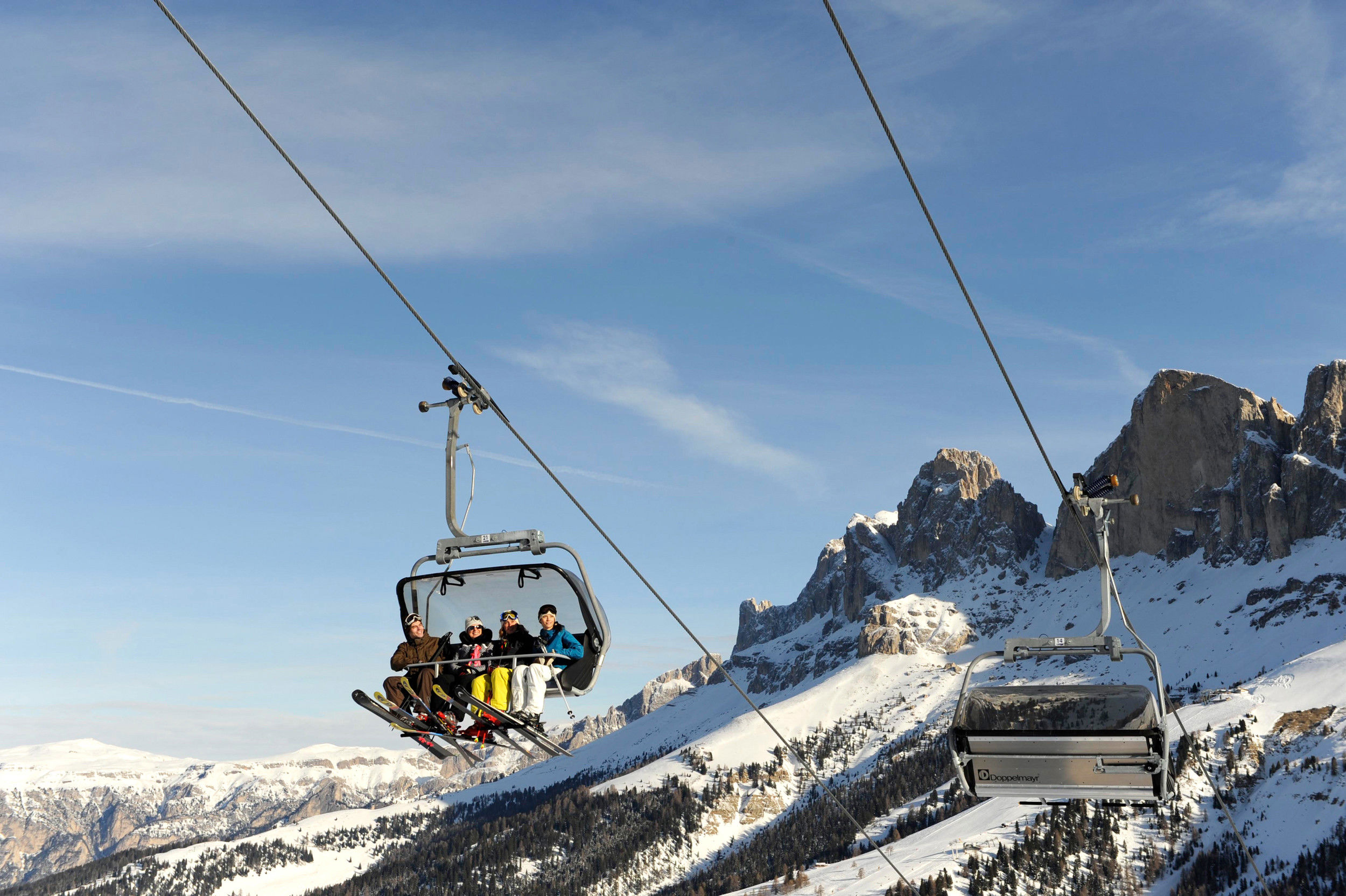 4 skiers sitting in the chairlift. In the background you can see the 3 Peaks.