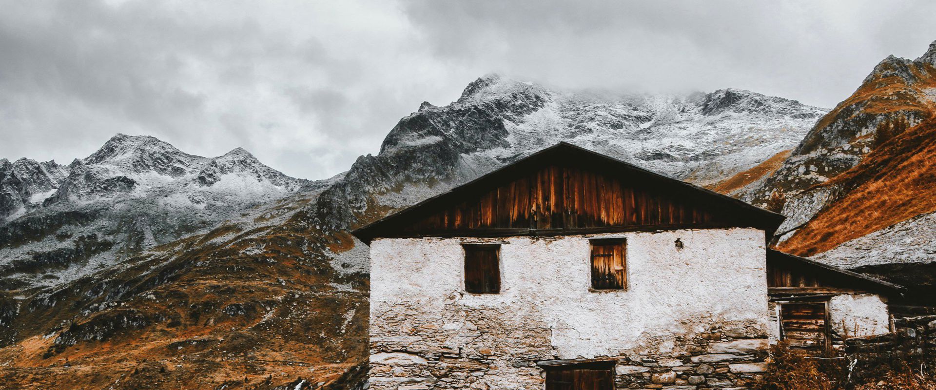 Nature Park Rieseerferner-Ahrn Old, abandoned mountain hut surrounded by snow-covered mountain peaks.