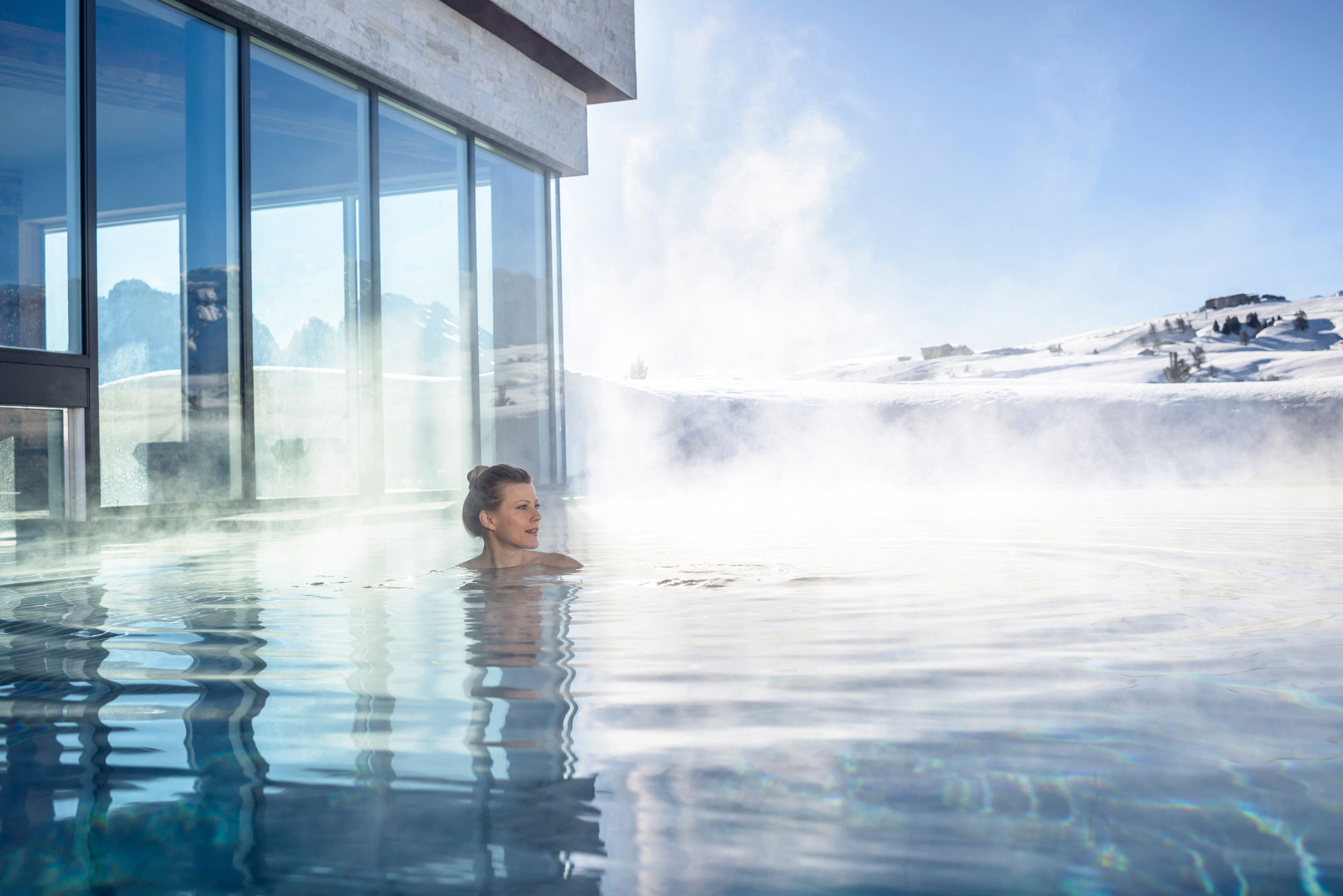 A woman swims in the warm, steaming outdoor pool.
