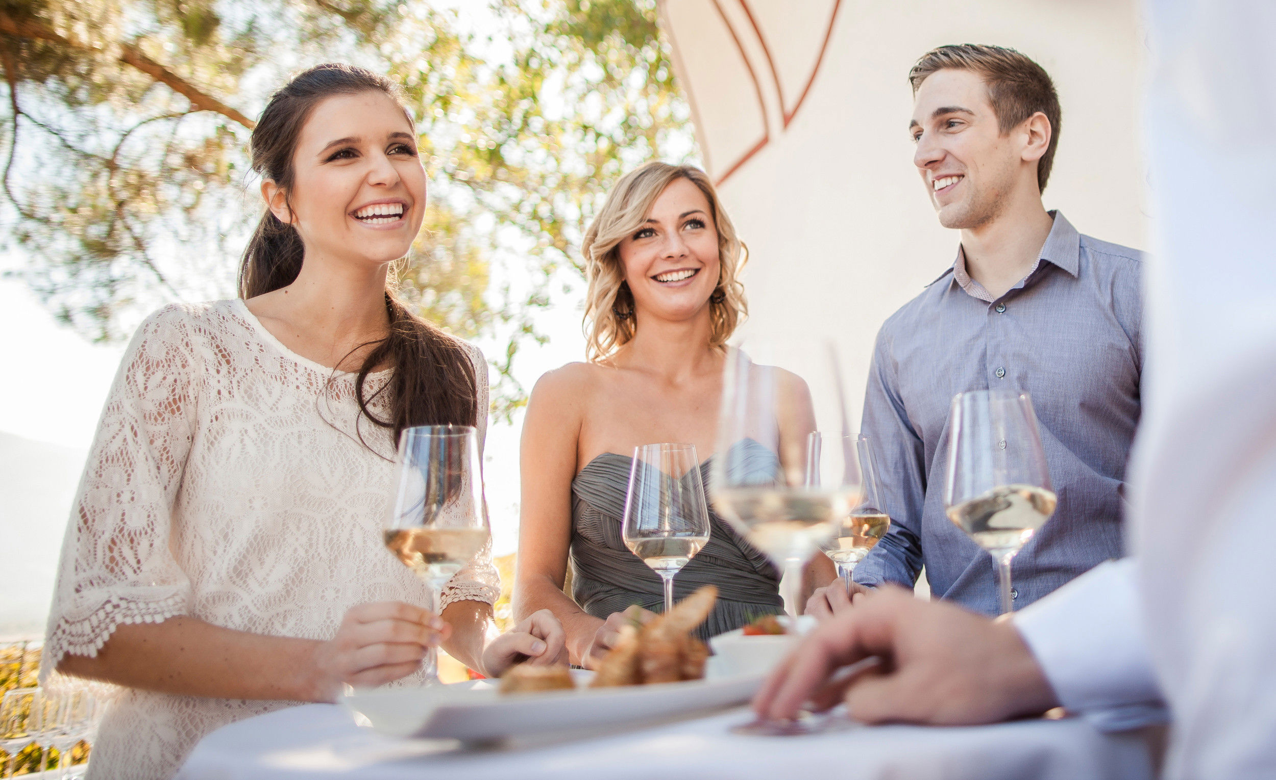 Young people stand around a table with a glass of white wine in their hands.