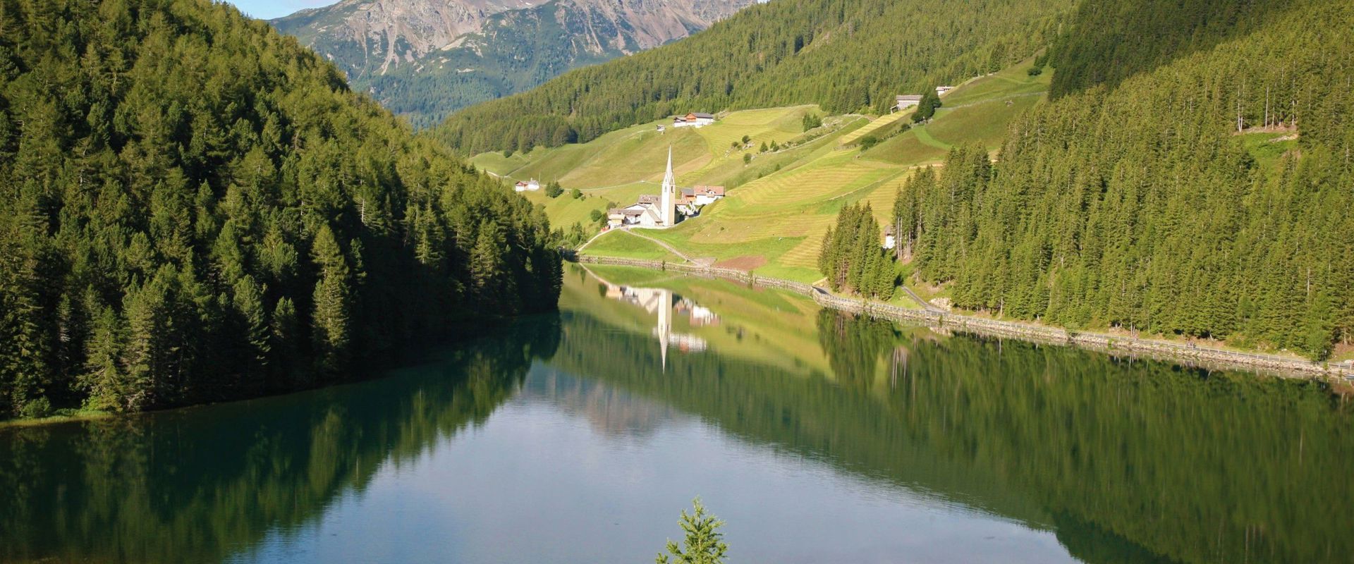 Idyllically situated lake with mountain panorama and view of a small church.