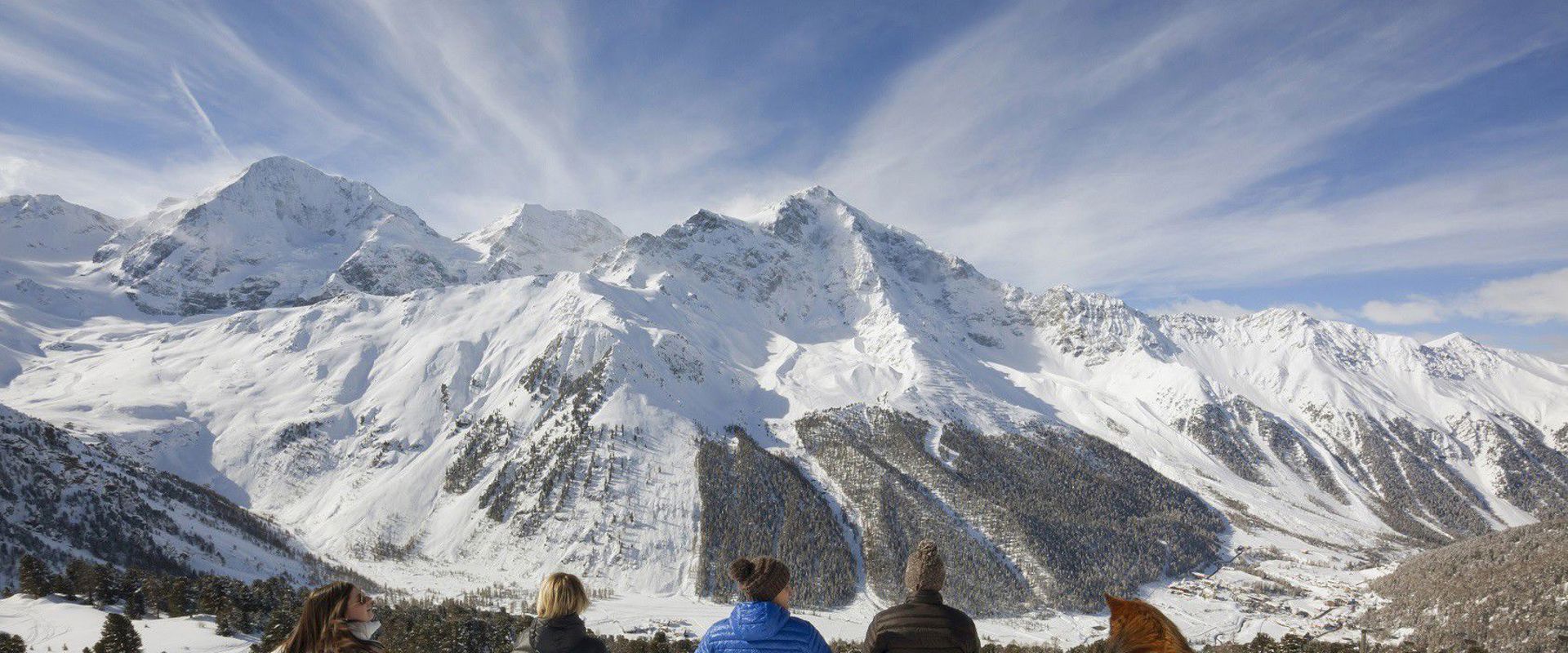 National Park Stilfserjoch in winter Group of young girls with dog sitting in the snow at the top of the mountain, admiring the mountain peaks.