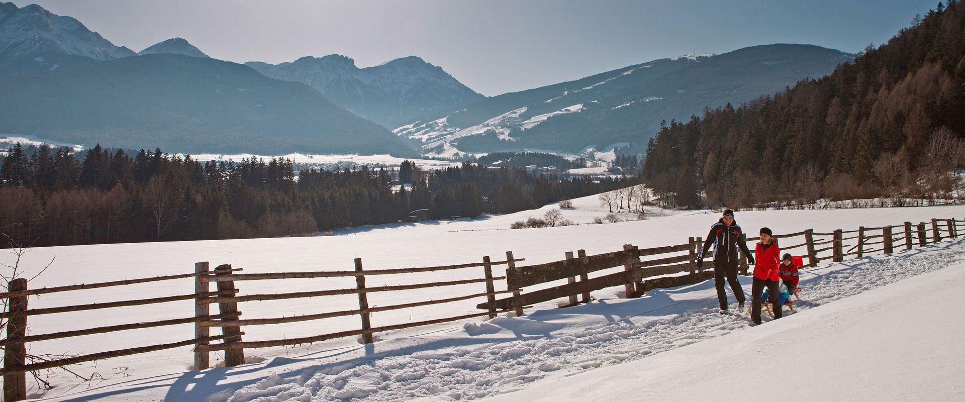 Winter in Rasen-Antholz. Man and woman pulling two children on sledges through sunny winter landscape.