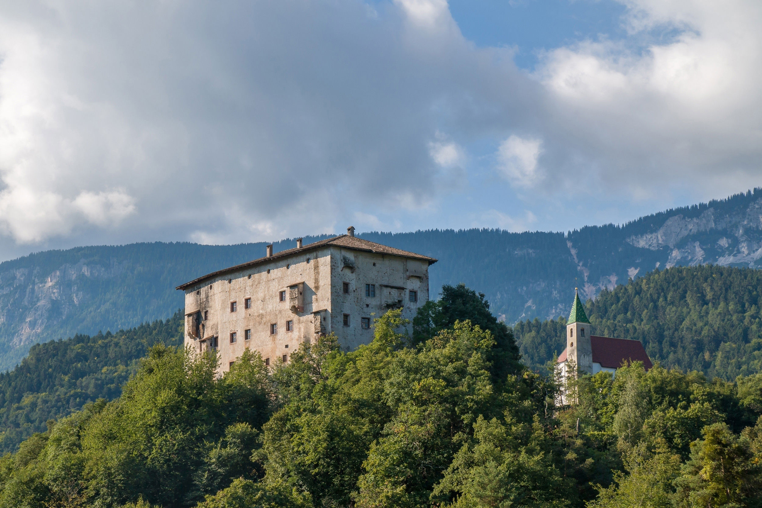 Castle on a wooded hill with a church next to it.