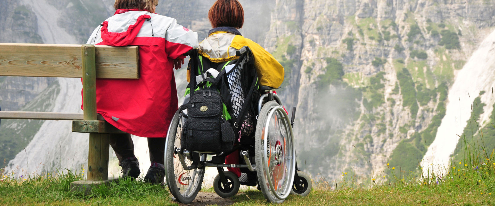 Hiking without barriers A man is sitting on a wooden bench, while the woman next to him is sitting in a wheelchair.