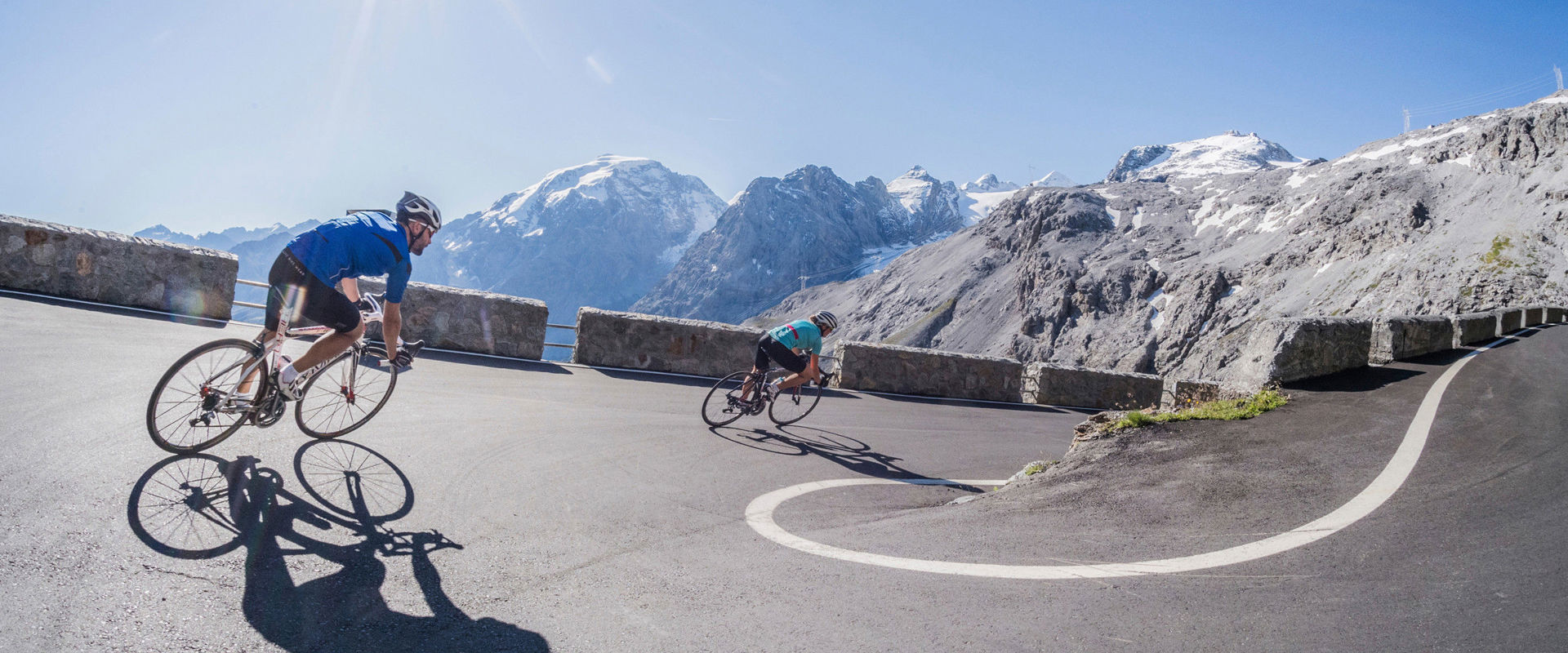 2 cyclists ride down a winding pass road.