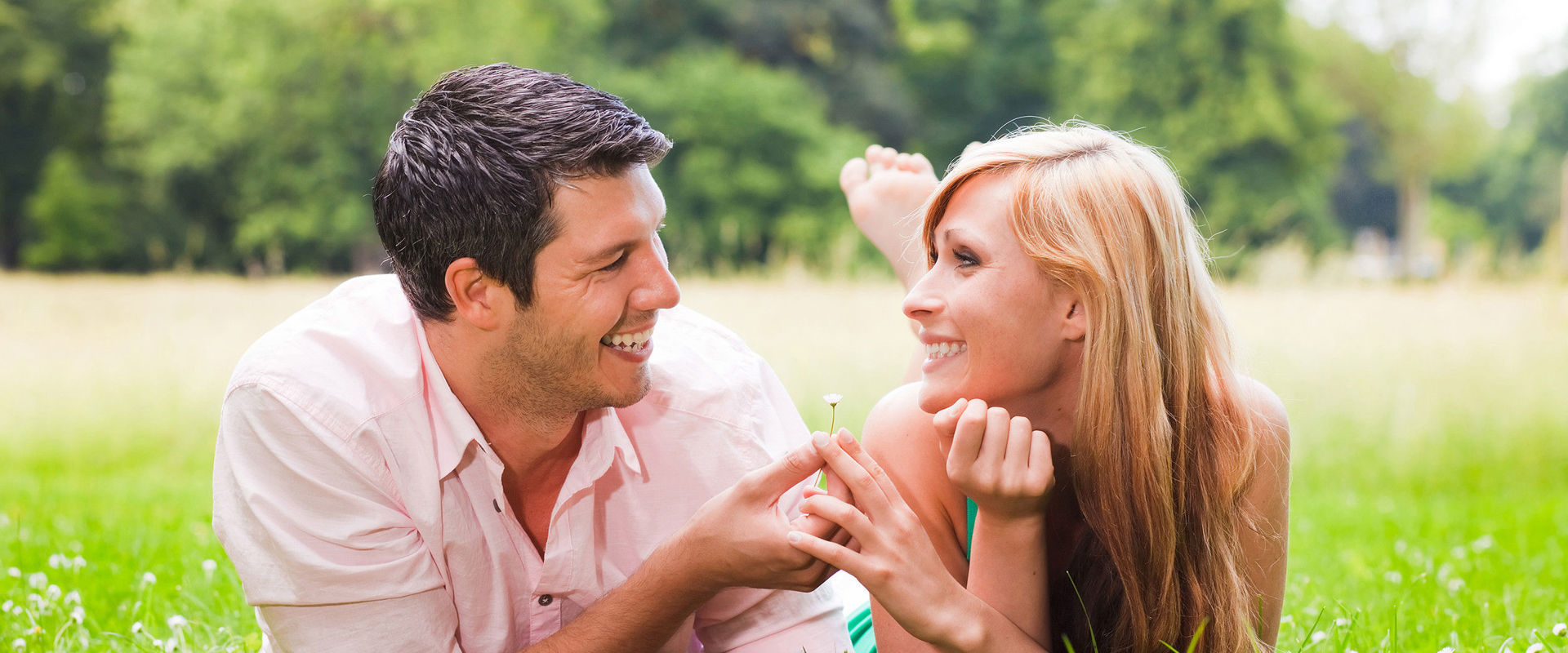 A couple in love lie in a summer meadow. The man gives the woman a flower.