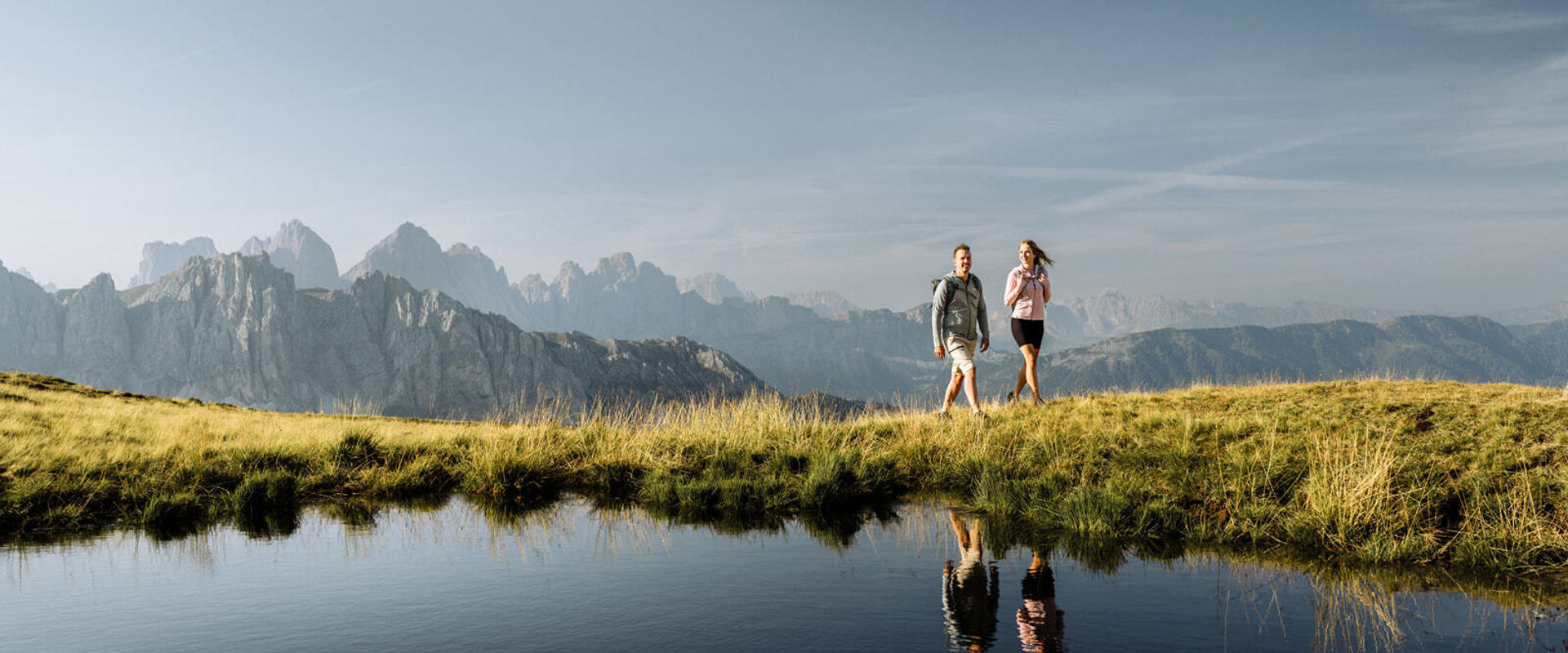 Hikers reflected in a mountain lake with mountain peaks in the background