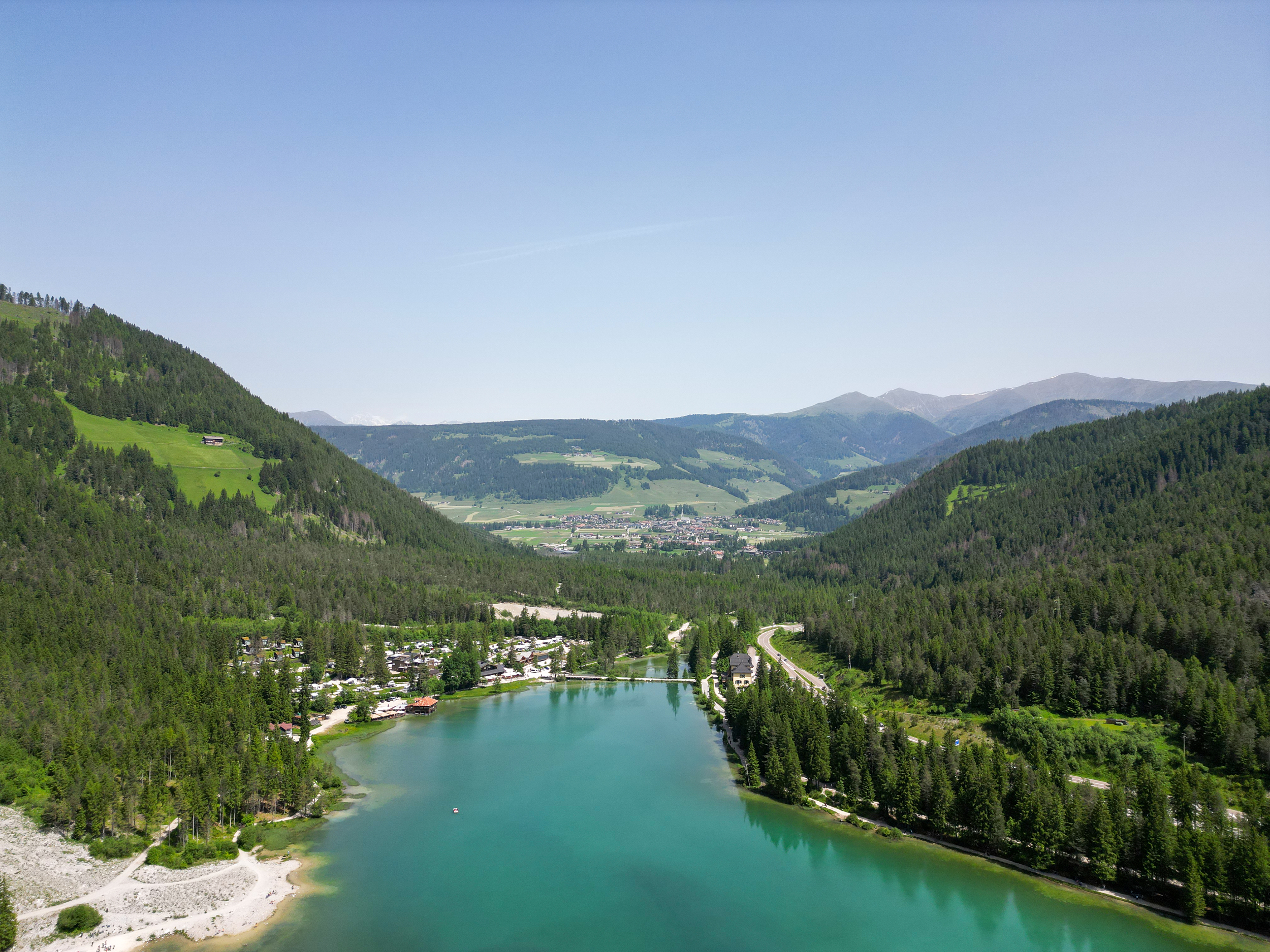 Lake framed by forests and campsite, mountain landscape with village in the background