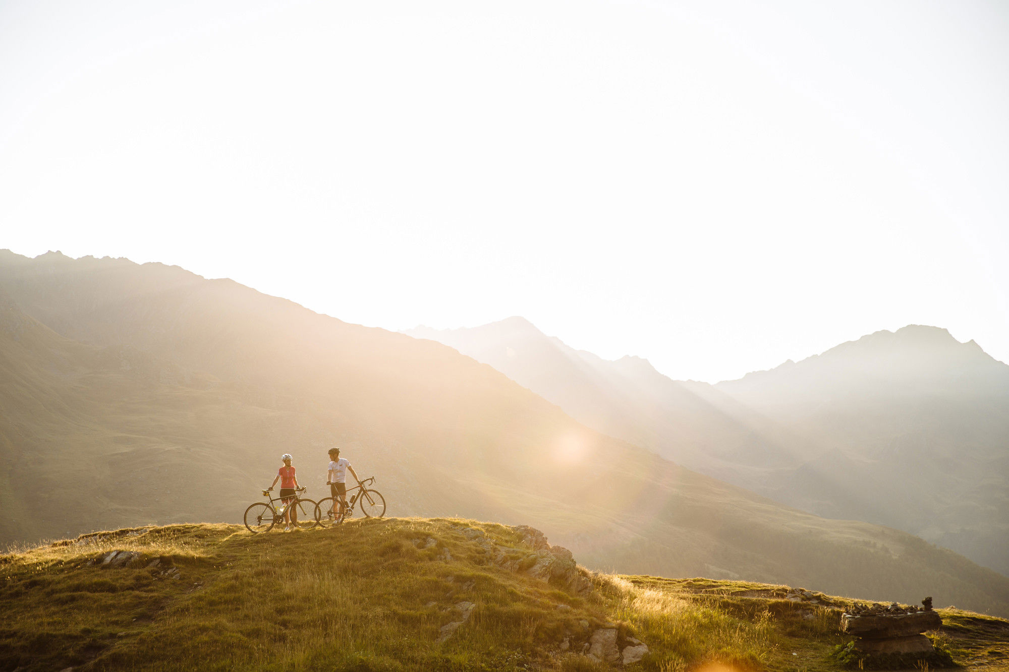 2 cyclists stand in the middle of a breathtaking mountain landscape.