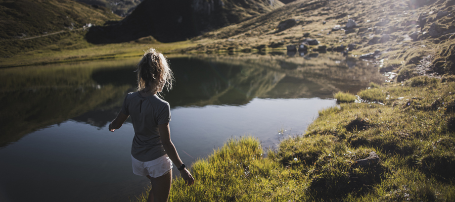 A woman is walking through the grass on the shore of a South Tyrolean mountain lake.