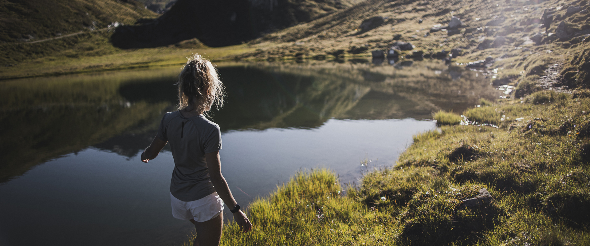 A woman is walking through the grass on the shore of a South Tyrolean mountain lake.