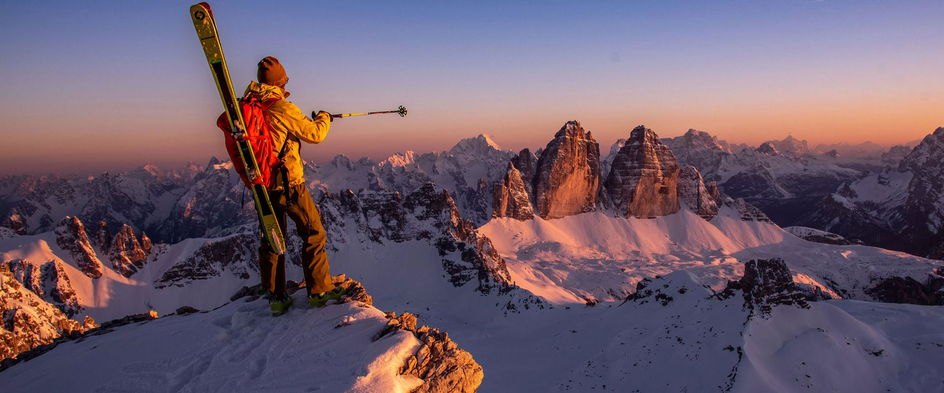 Ski mountaineer admires the Three Peaks after climbing to the summit with his skis on his shoulders.