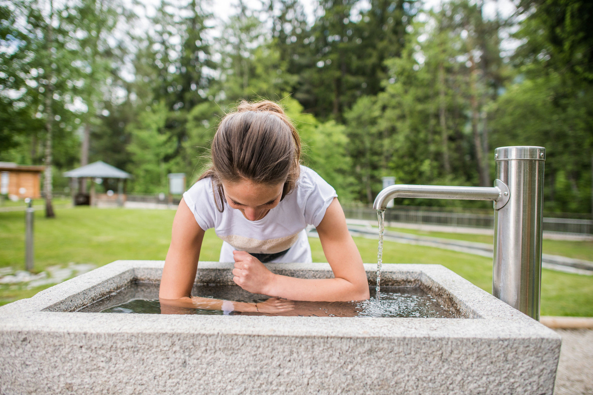 Woman dipping her forearms into the cold water of a fountain.