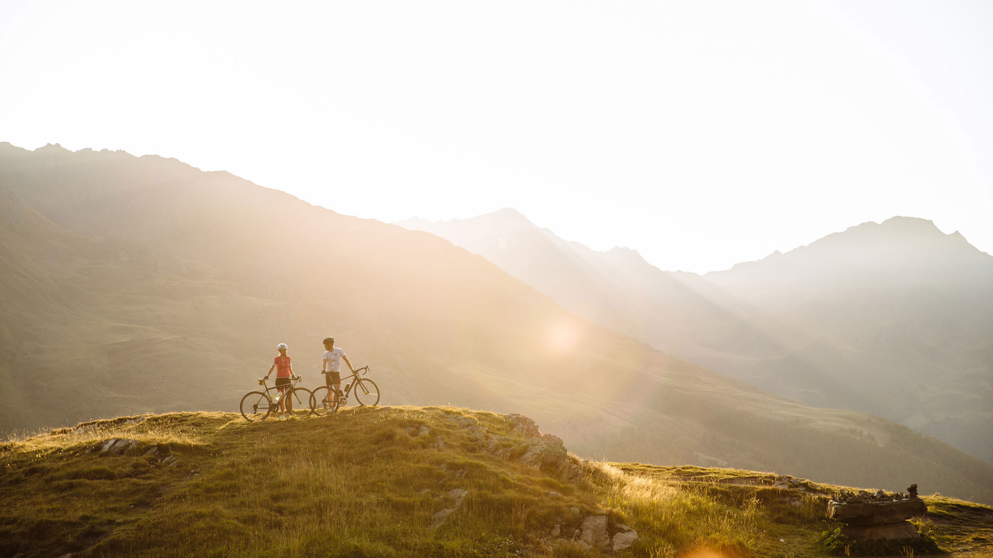 Two cyclists stand on the hill with their bikes and enjoy the morning sun.