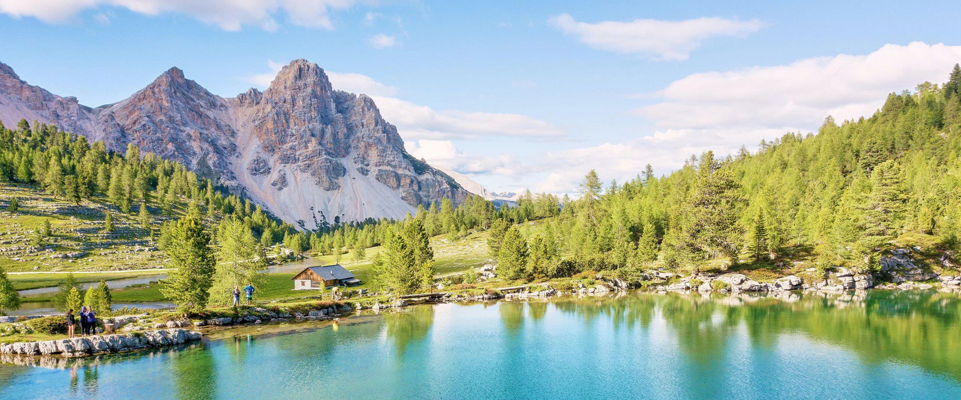 Nature Park Fanes-Sennes-Prags Turquoise blue lake surrounded by green meadow and trees with a view of the Dolomites.